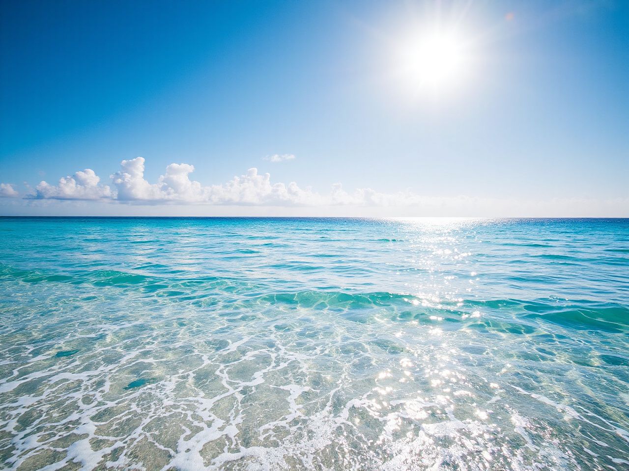 Sunlit tropical beach with clear blue waters and gentle waves under a bright sky