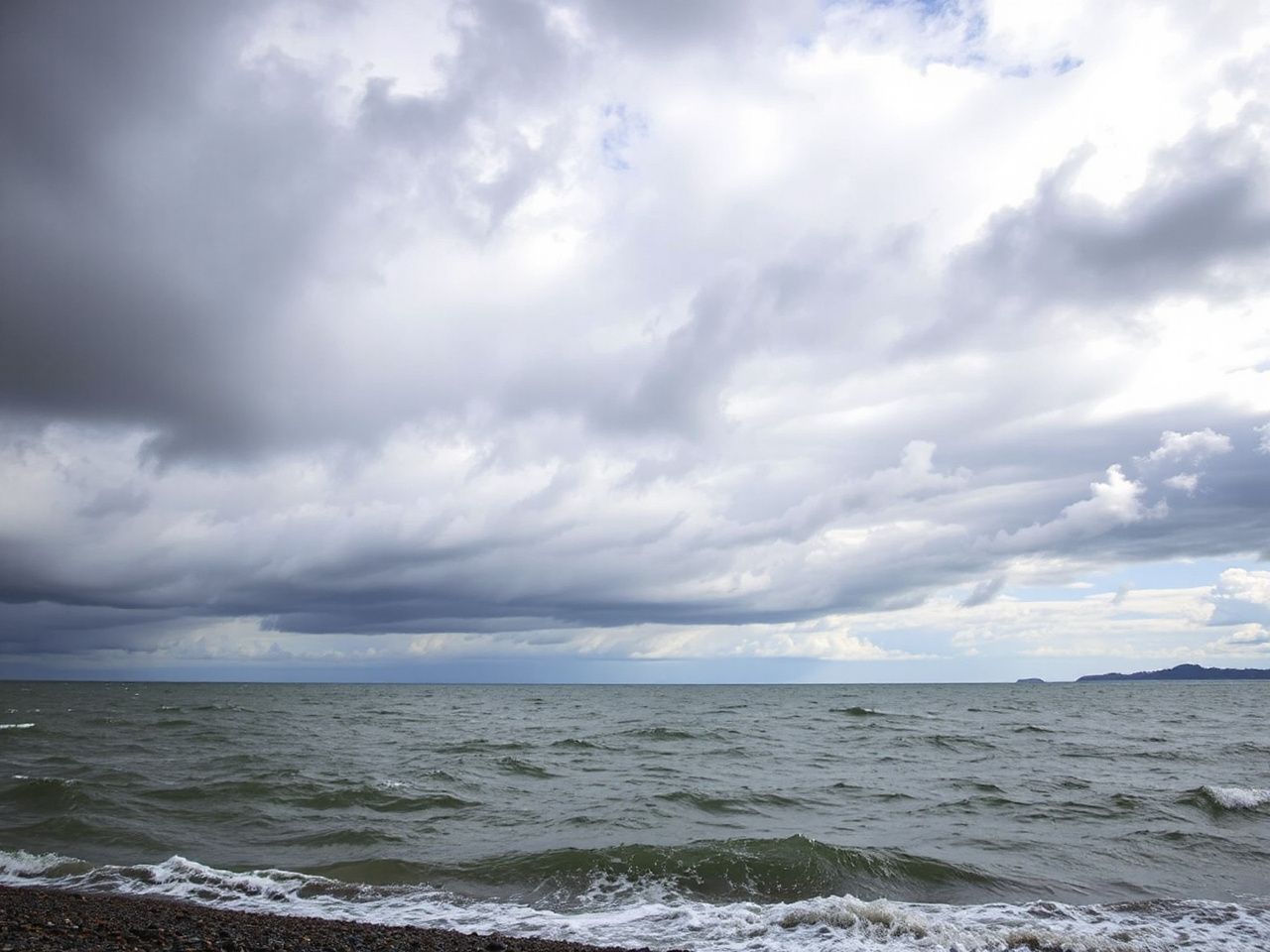 Dark clouds rolling over the bay with choppy water and windswept shoreline under a moody sky