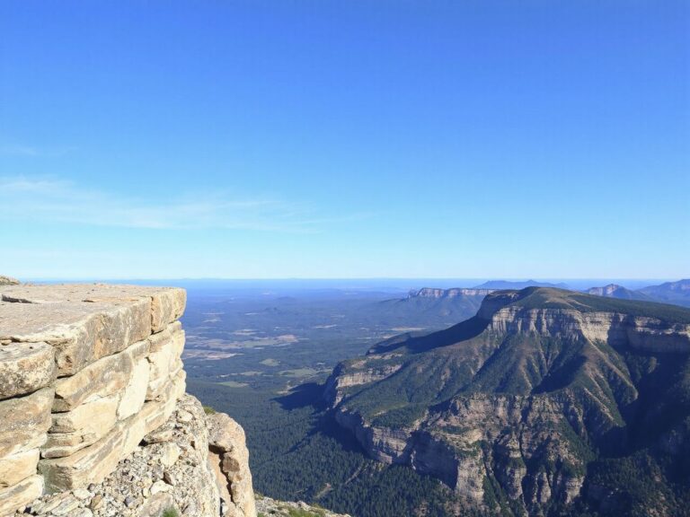 A rugged cliff edge overlooking a vast valley beneath a clear blue sky, perfect for base jumping