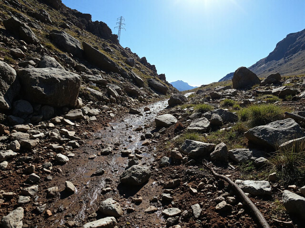 Rocky mountain path strewn with wet mud and scattered stones under bright daylight, perfect for rugged trail running