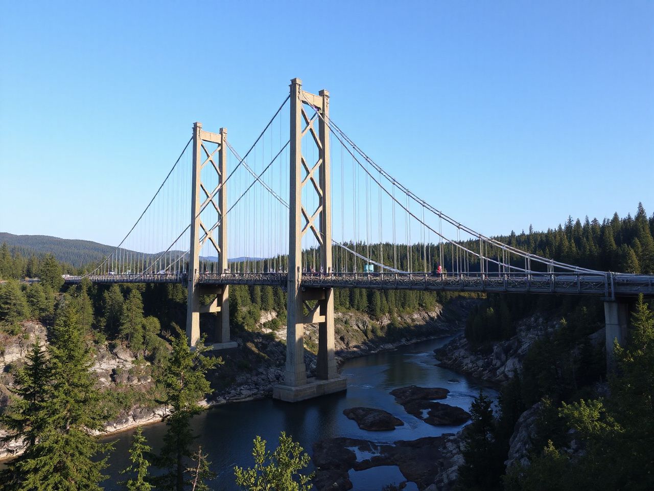A towering suspension bridge arching over a deep river gorge, surrounded by lush green forest and clear blue sky