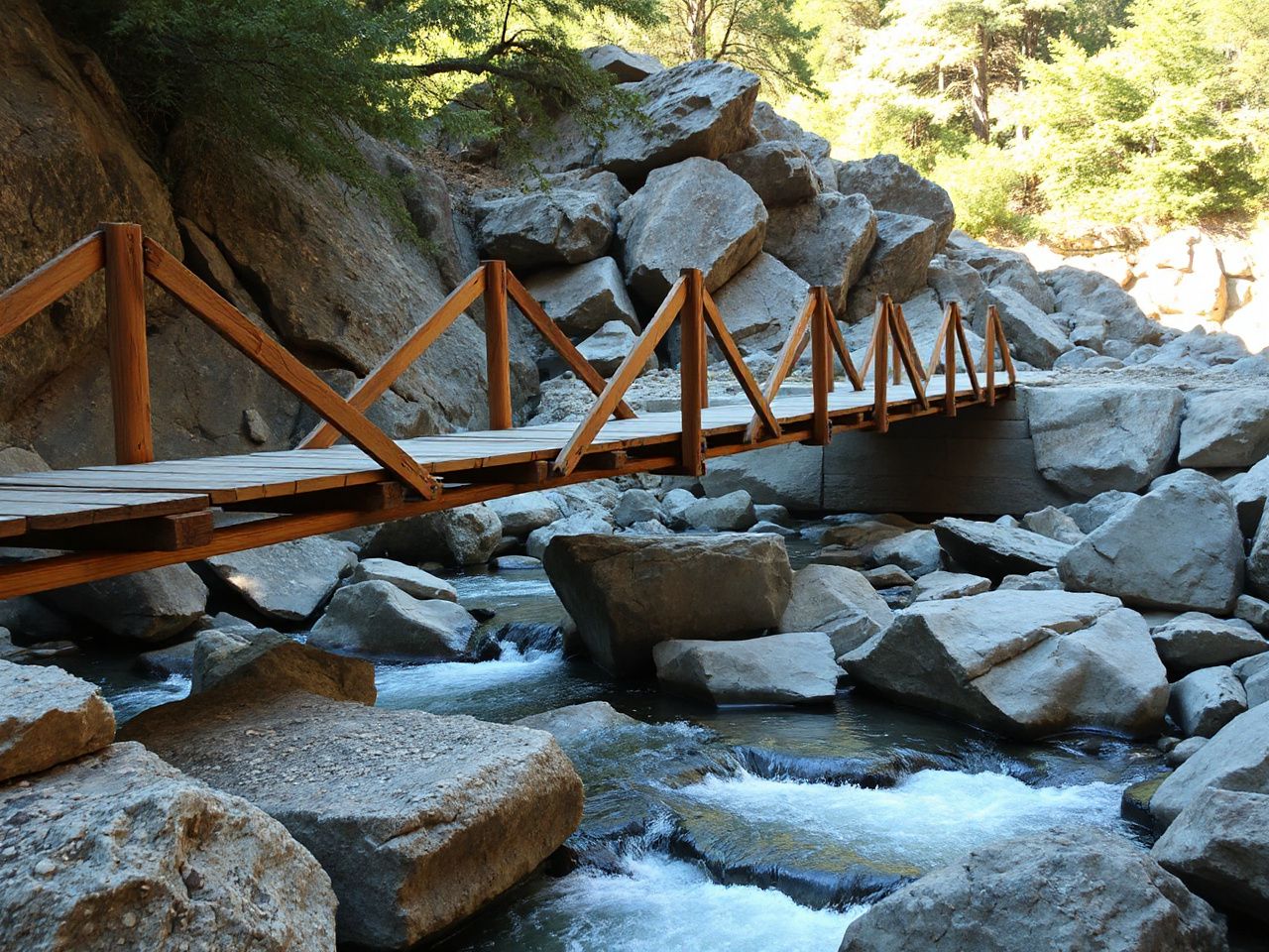 A sturdy wooden bridge spanning a rocky river, emphasizing reliable natural anchor points in outdoor adventures