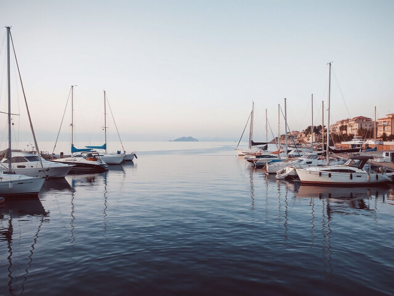 A quiet Mediterranean harbor at dawn with moored boats and calm, reflective water under clear skies
