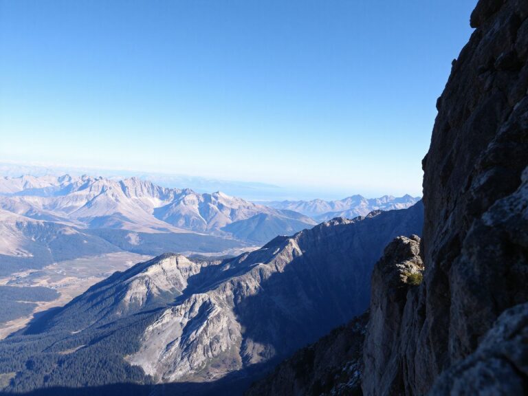 A dramatic mountain cliff edge overlooking a vast valley under a clear blue sky, perfect for wingsuit launching