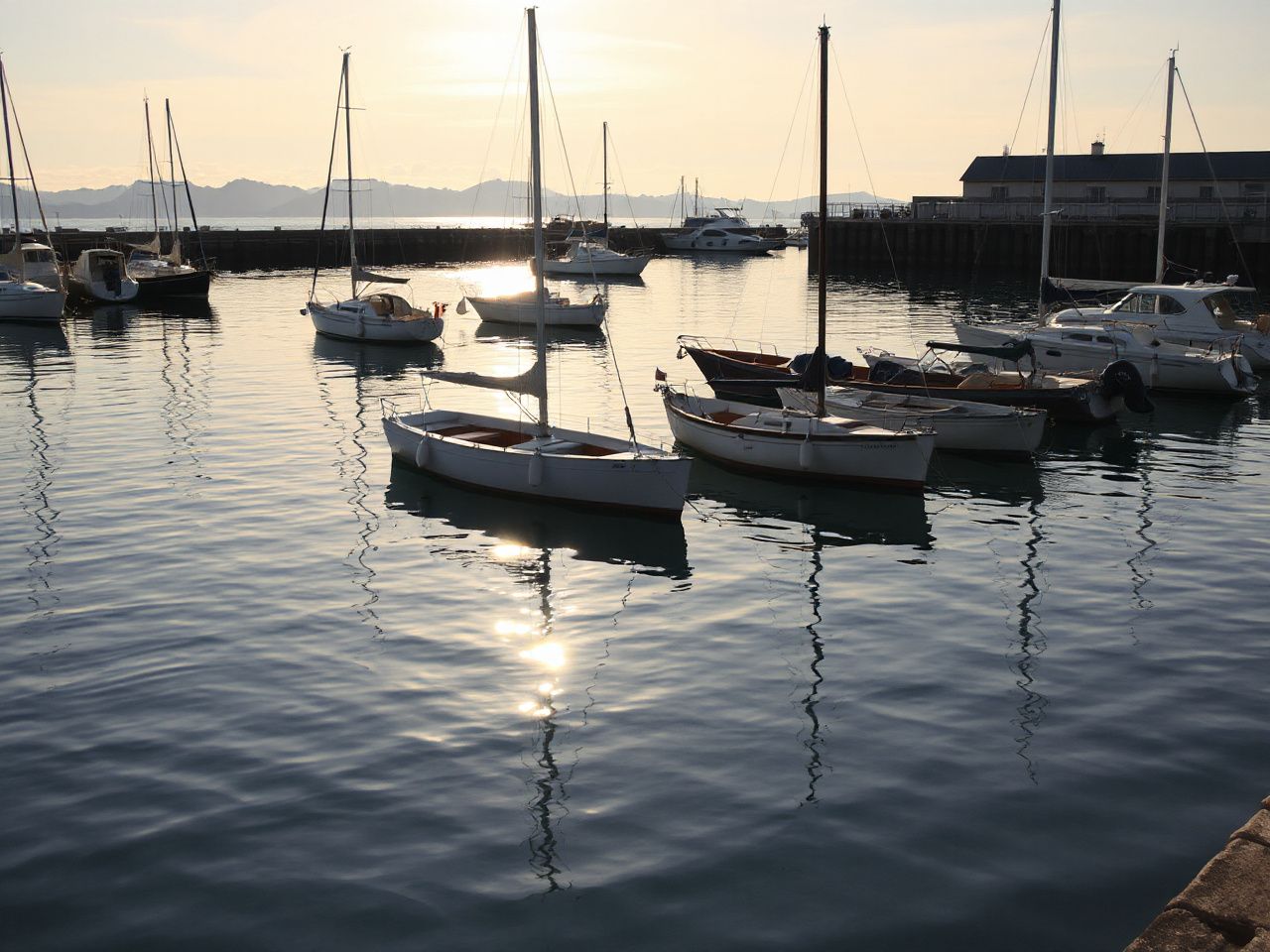 Quiet harbor at midday with boats anchored gently, reflecting calm water and shifting sunlight patterns