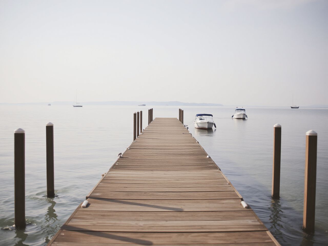 A quiet, empty pier stretching into calm waters with moored boats and soft morning light