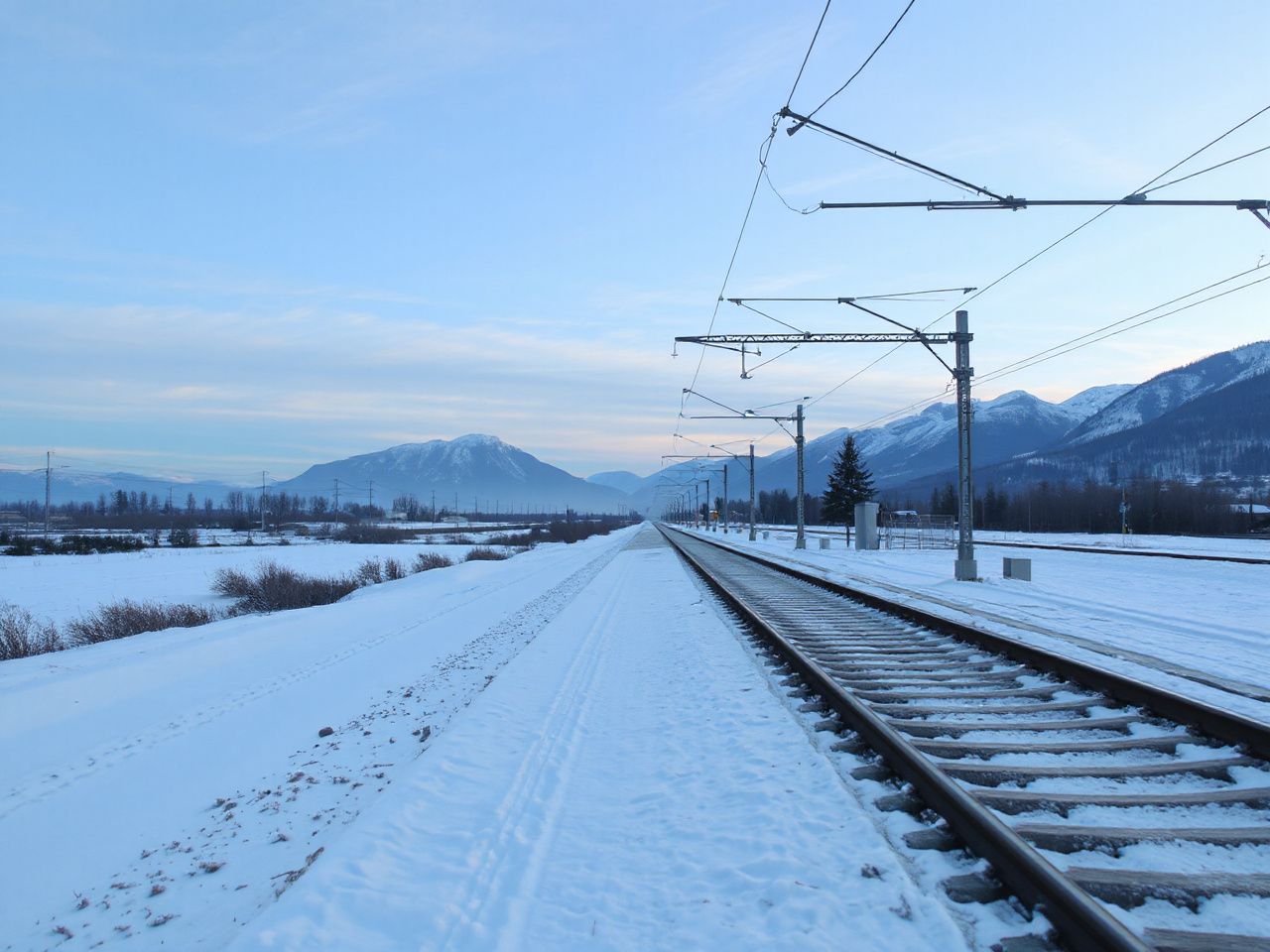 A quiet, snow-dusted railway platform at dawn, with distant mountains under a pale blue sky