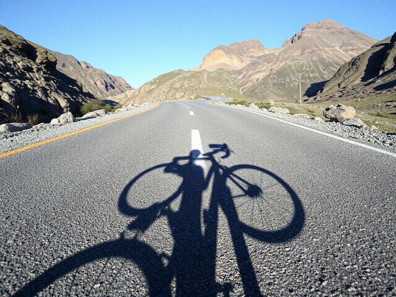 A rugged mountain road with a cyclist’s shadow cast on the pavement, symbolizing multi-sport insole use