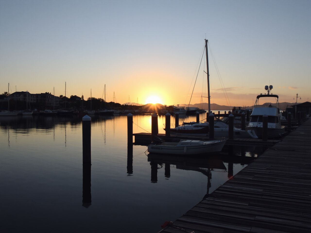 A calm harbor at sunrise with several boats docked quietly along the wooden piers