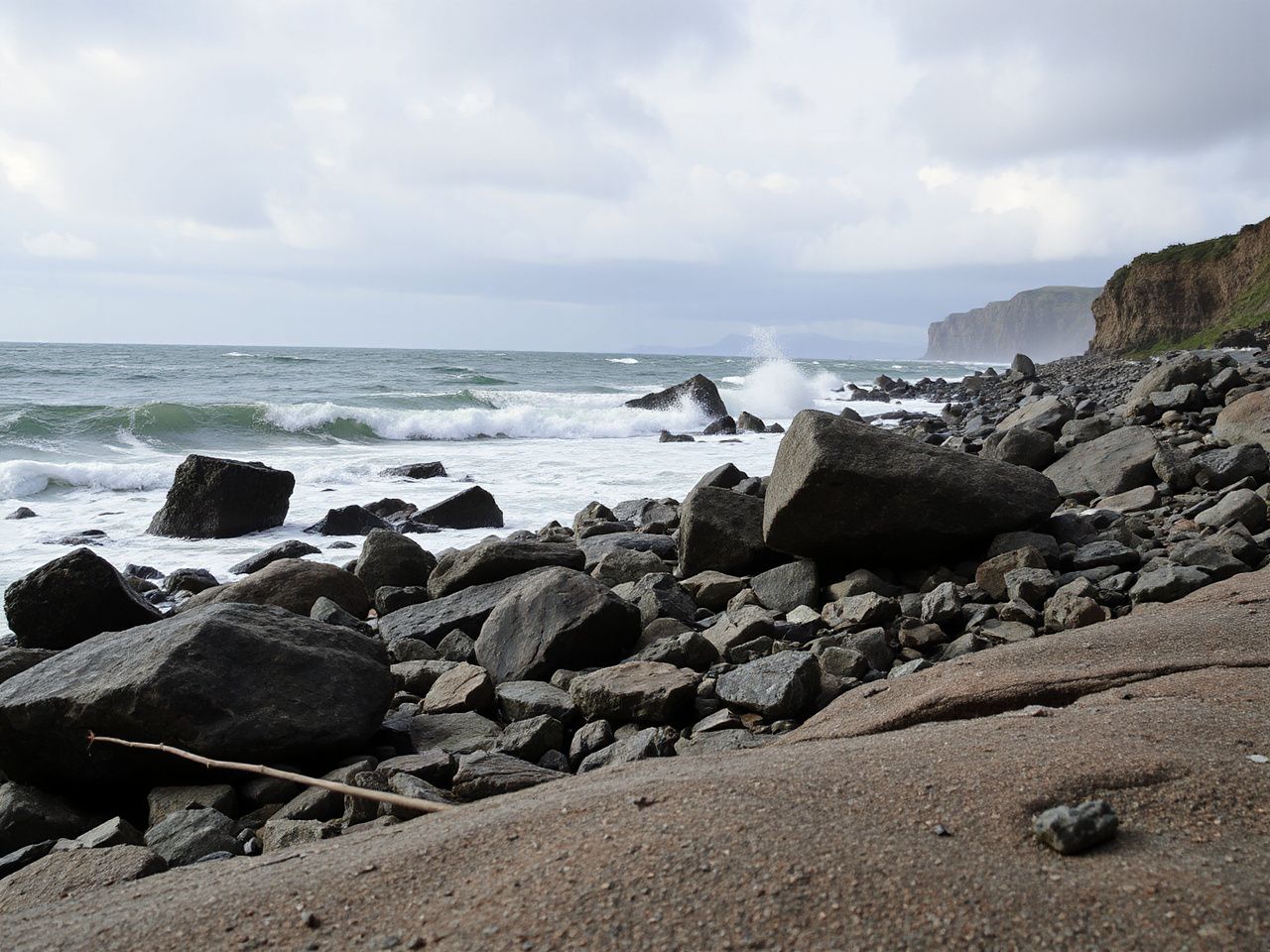 Wind-swept rocky shoreline under cloudy skies, demonstrating the need for durable, weather-resistant outer shells