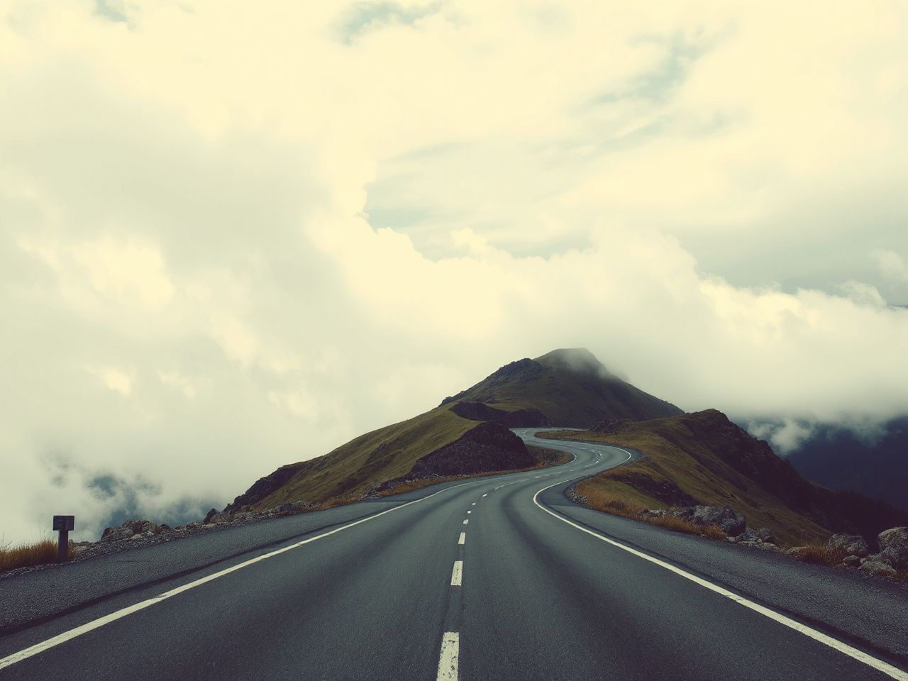 A winding mountain road disappearing into a cloudy sky, illustrating the unpredictability of travel plans